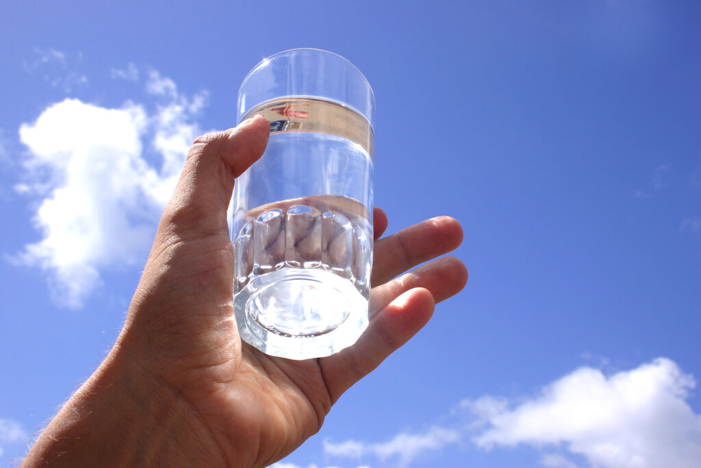 Hand holding glass of pure Artezia water up to the sky