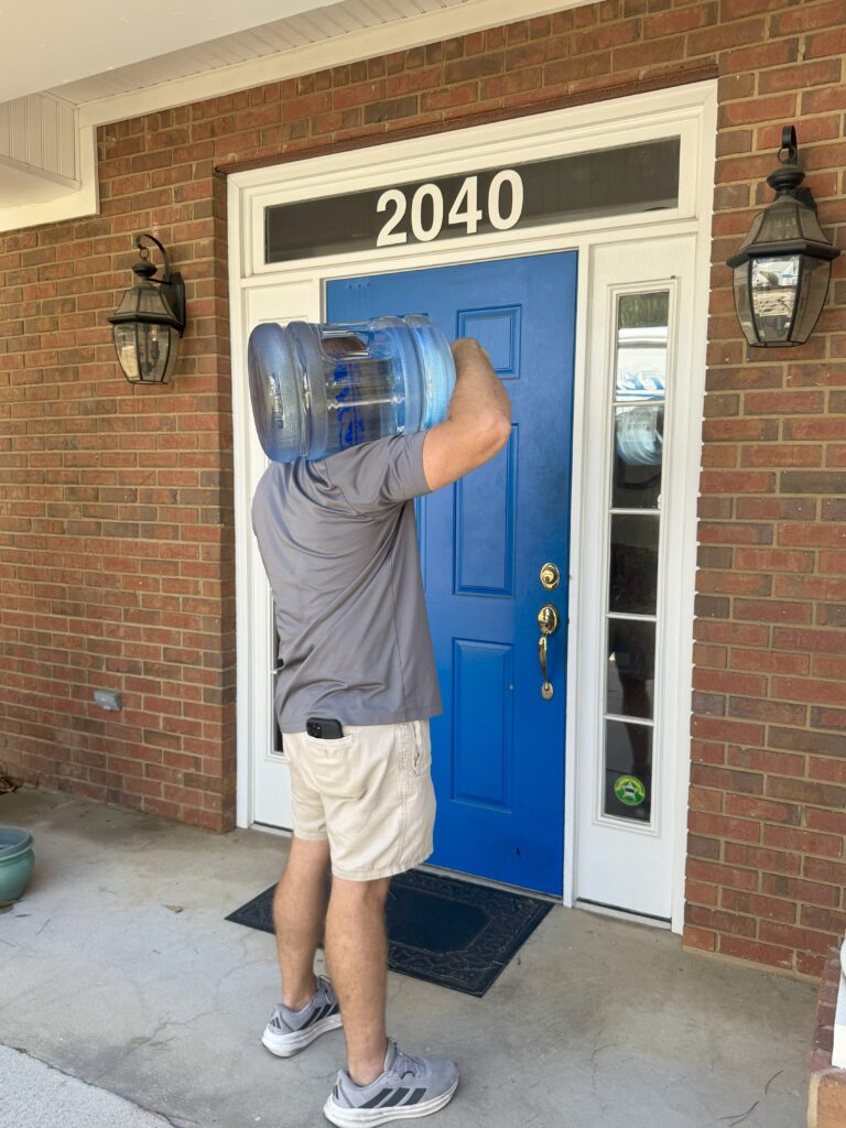 Trevor from Artezia Water delivering a 5-gallon bottle of Artezia Water to the front door of a home for home water delivery